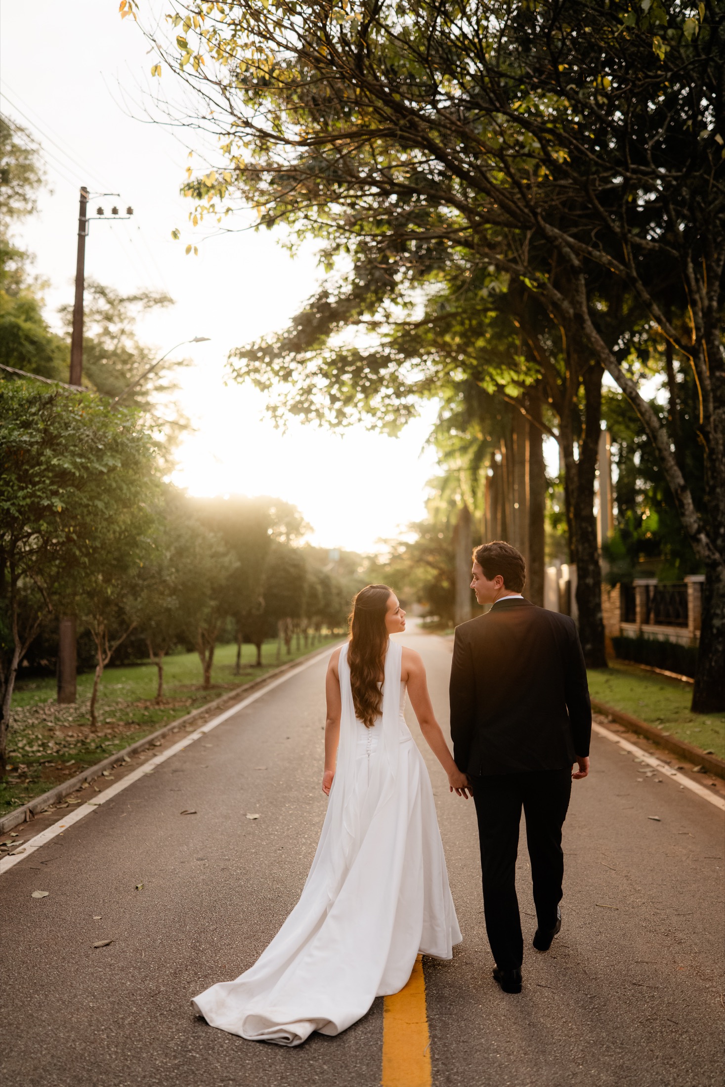 Nicolas e Mariane caminham juntos por uma estrada arborizada.