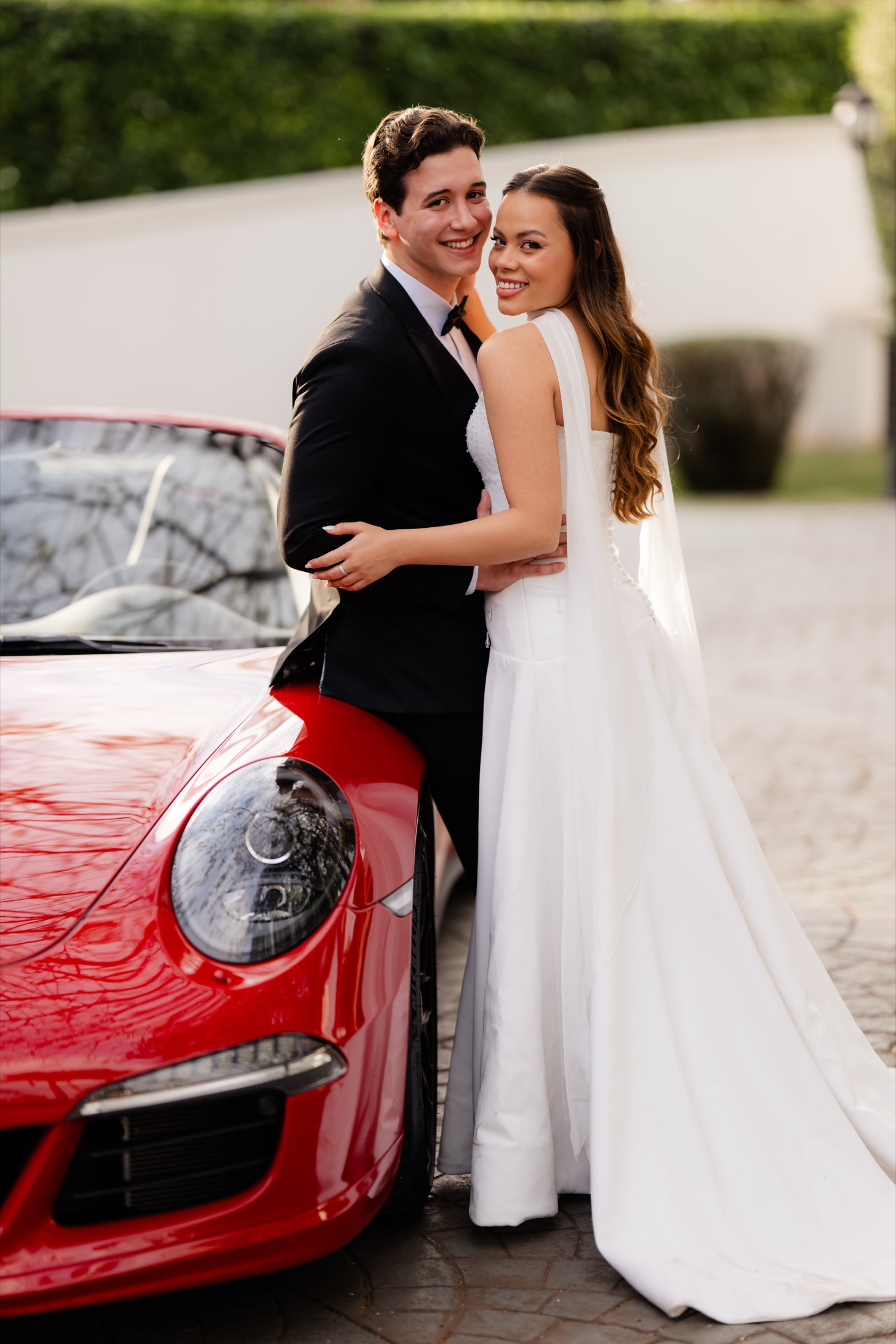 Nicolas e Mariane juntos ao lado de um carro vermelho.